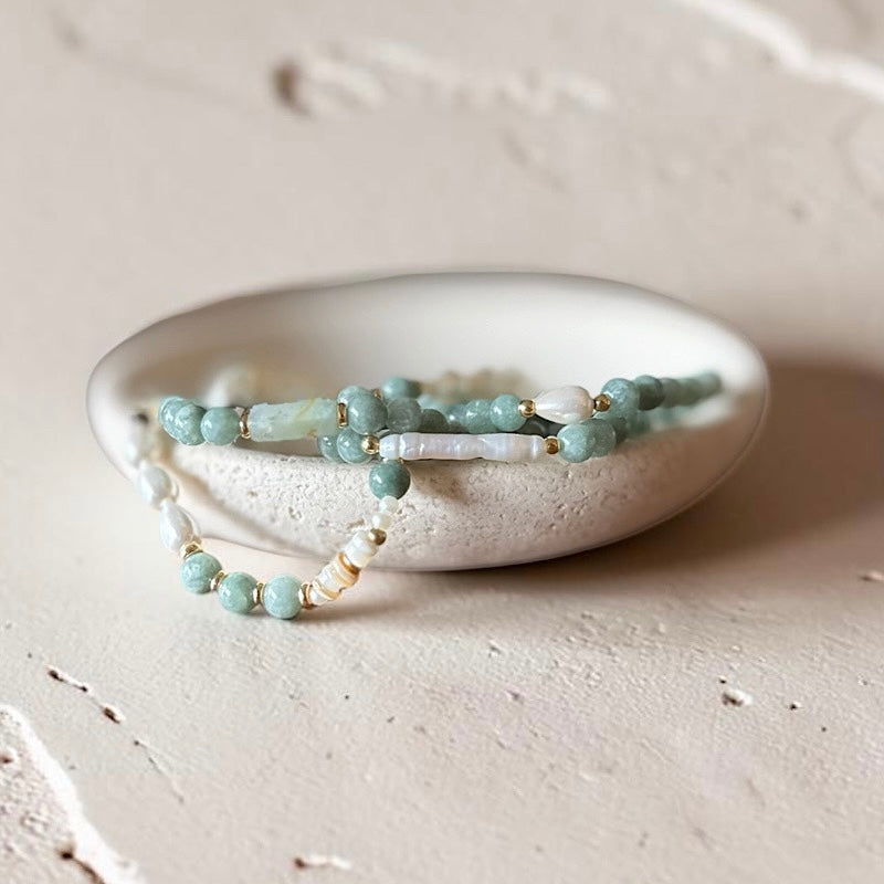 A stack of beaded bracelets in blue, peach, and white, displayed on a small round ceramic dish against a textured off-white background.