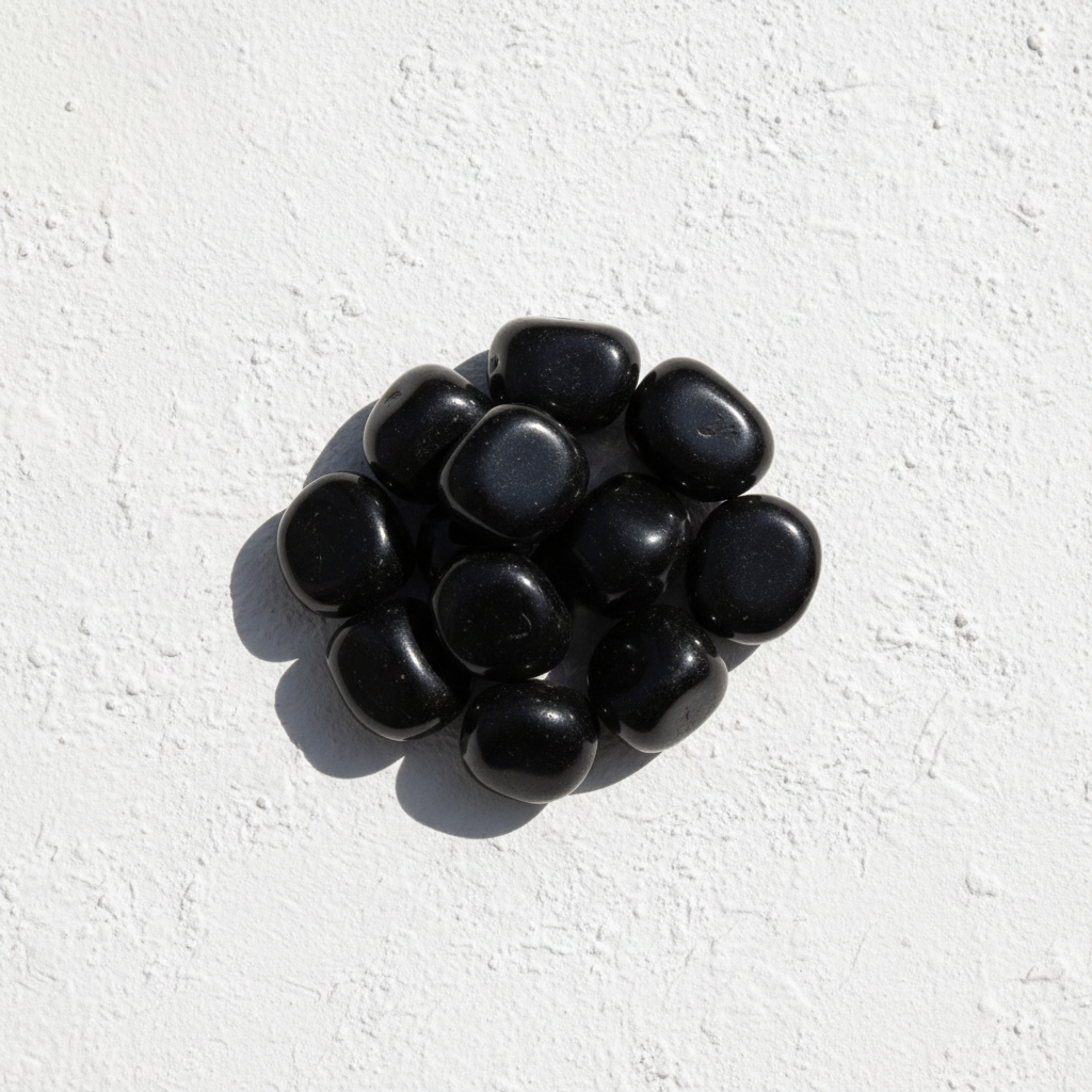 Black onyx tumbled stones at medium-large size on white textured background