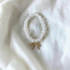 A beaded bracelet made of clear faceted round beads with a small gold bow charm, displayed on a soft white fabric background.
