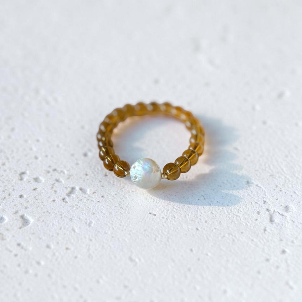 A beaded bracelet with translucent amber-brown beads and a single white iridescent pearl-like bead, photographed on a light textured white surface.