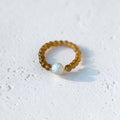 A beaded bracelet with translucent amber-brown beads and a single white iridescent pearl-like bead, photographed on a light textured white surface.