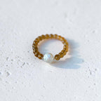 A beaded bracelet with translucent amber-brown beads and a single white iridescent pearl-like bead, photographed on a light textured white surface.