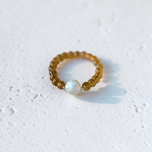 A beaded bracelet with translucent amber-brown beads and a single white iridescent pearl-like bead, photographed on a light textured white surface.