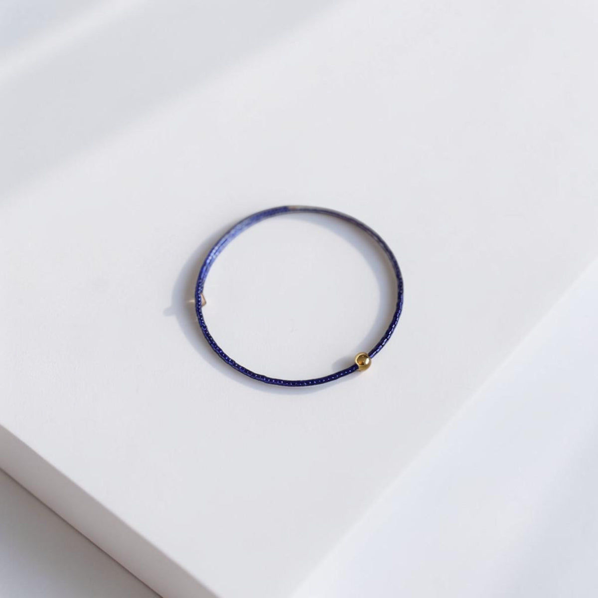 A thin dark purple blue beaded bracelet with a small gold bead accent, displayed on a clean white surface.