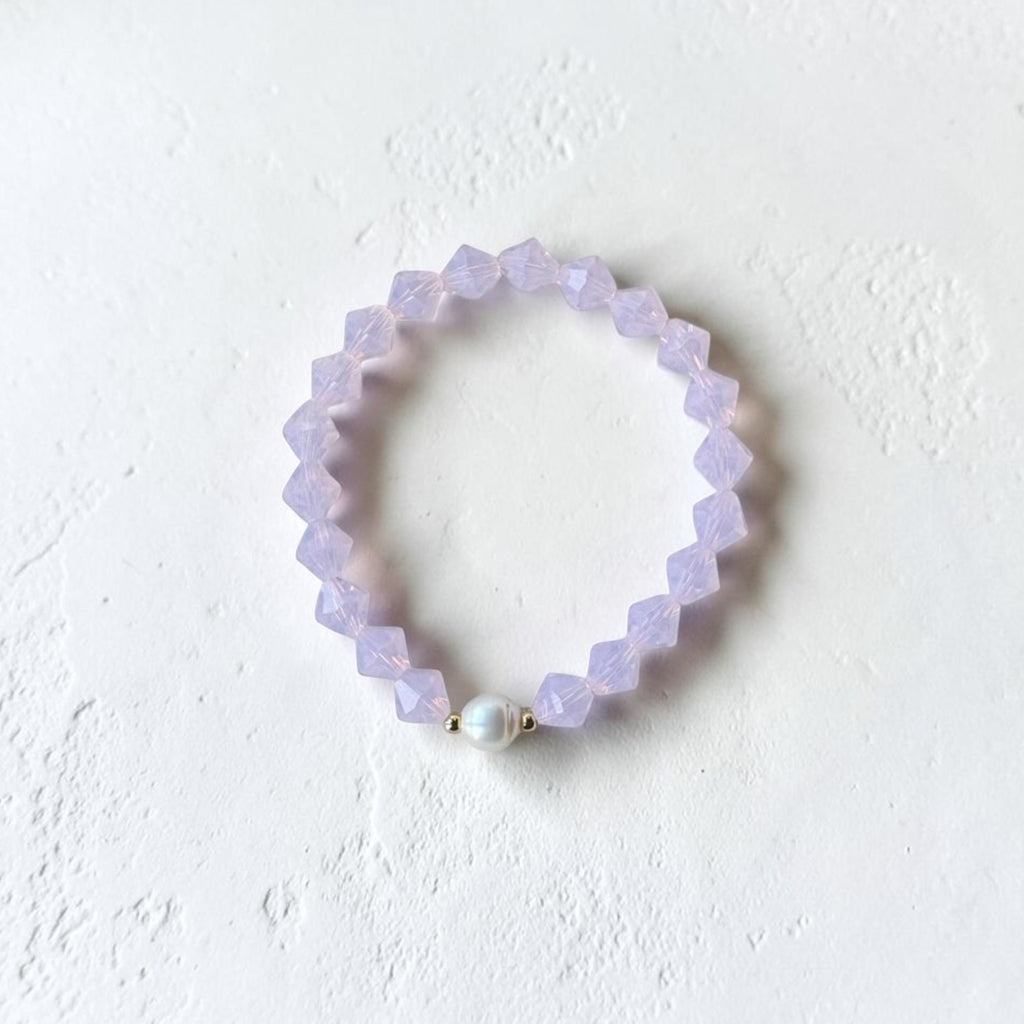 A light purple beaded stretch bracelet with a single white pearl accent bead, displayed on a textured white surface.
