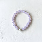 A light purple beaded stretch bracelet with a single white pearl accent bead, displayed on a textured white surface.