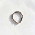 A beaded stretch bracelet made of small, translucent smoky brown beads with a single white pearl accent, photographed on a white textured surface with soft shadows.