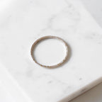 A thin seed bead wire bracelet in cream opal color with tiny gold dot accents along the band, resting on a white marble surface.