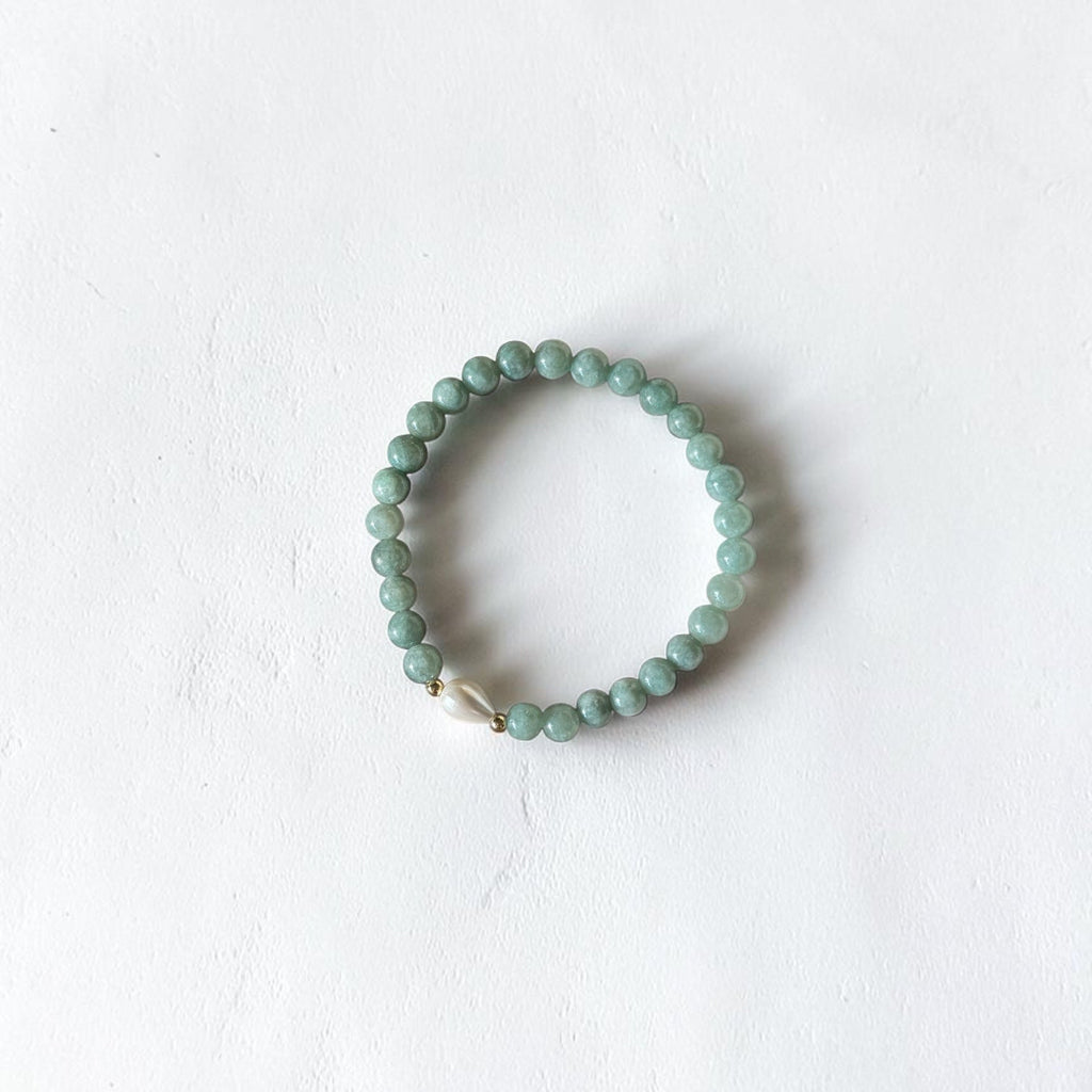 A beaded stretch bracelet made of small round light green beads with a small white shell accent, displayed on a textured white background.