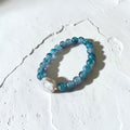 A beaded stretch bracelet featuring round light blue beads and a large, irregular white pearl-like accent bead, displayed on a textured white surface.