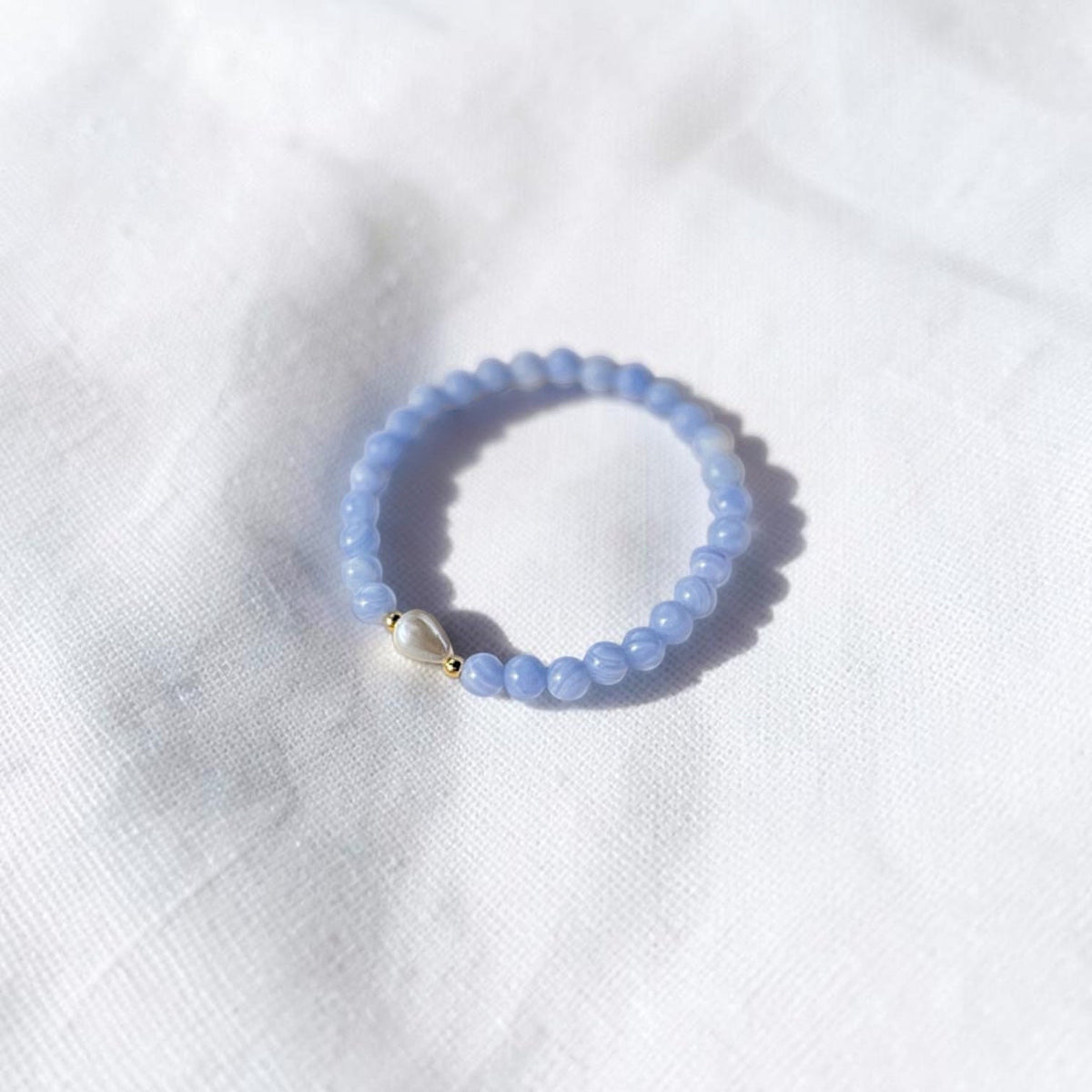 This is a 6mm light blue with subtle white swirls bracelet. The accent is a teardrop pearl With gold filled beads surrounding Pearl. 