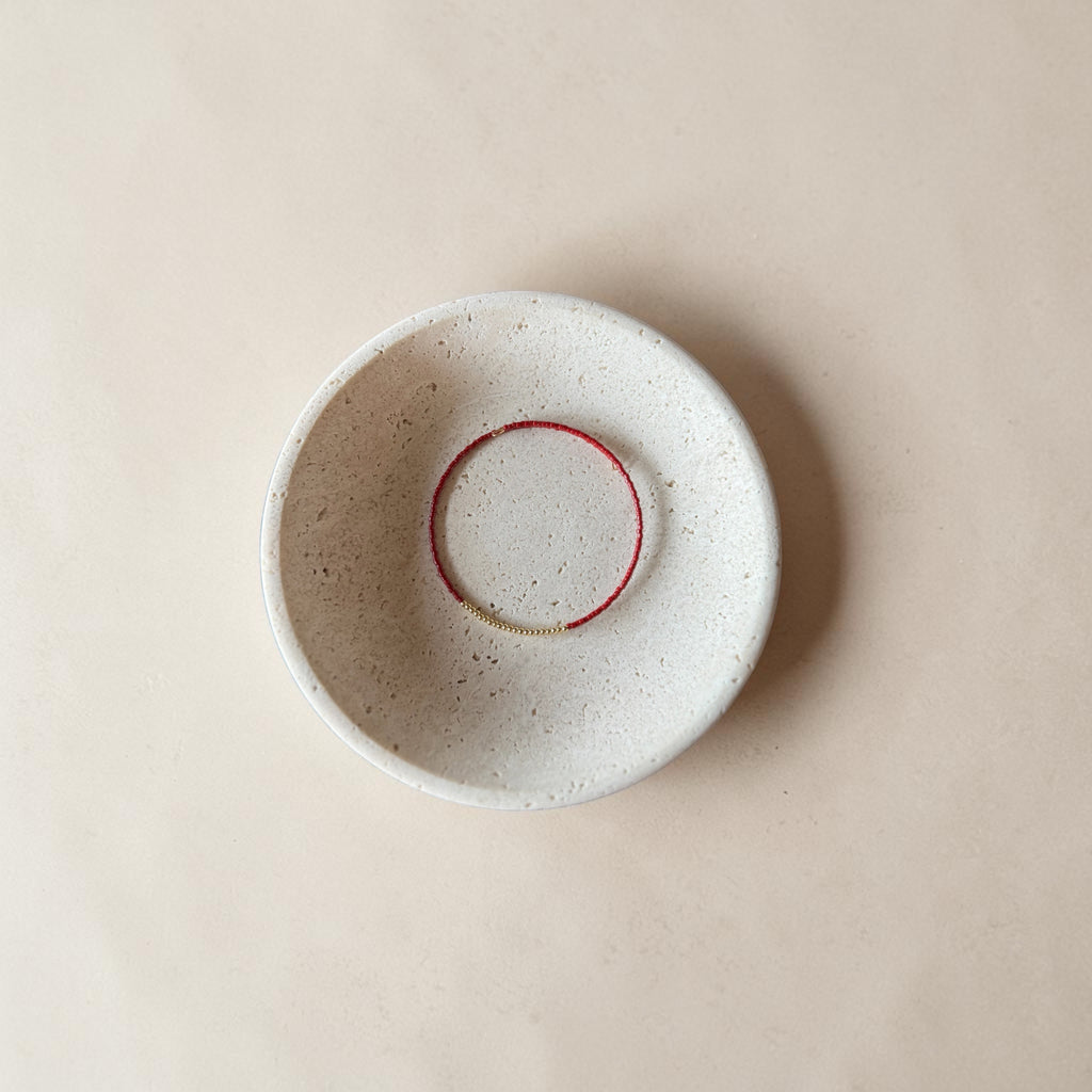A round, speckled ceramic bowl in a warm off-white glaze, featuring a contrasting red painted circular accent inside the rim, photographed from directly above on a matching beige background.