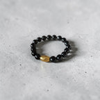 A beaded stretch bracelet featuring glossy black round beads and a single faceted gold accent bead, resting on a textured gray concrete surface.