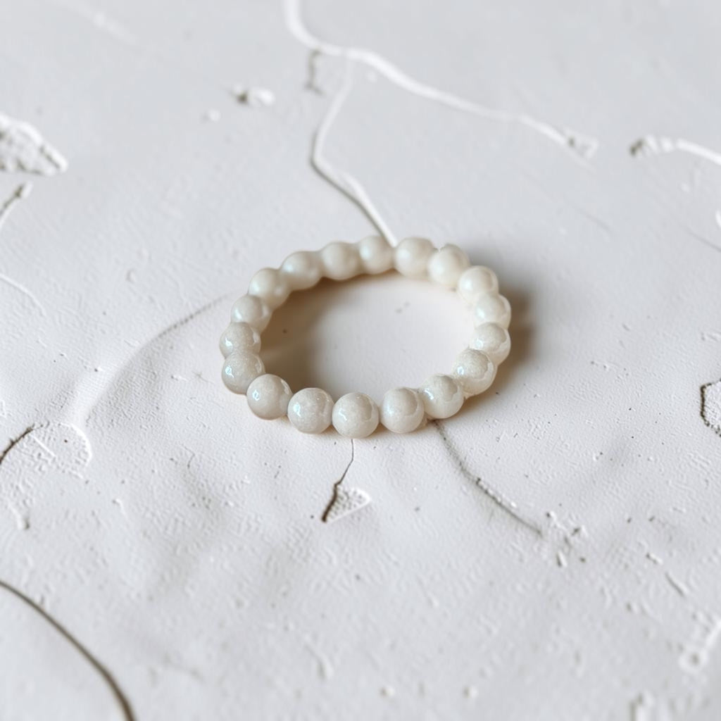 A beaded stretch bracelet made of small, round, off-white beads with a subtle pearlescent sheen, resting on a textured white surface.