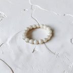 A beaded stretch bracelet made of small, round, off-white beads with a subtle pearlescent sheen, resting on a textured white surface.