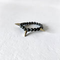 A beaded stretch bracelet featuring matte black round beads and two sharp, metallic gold spikes, resting on a textured white surface.