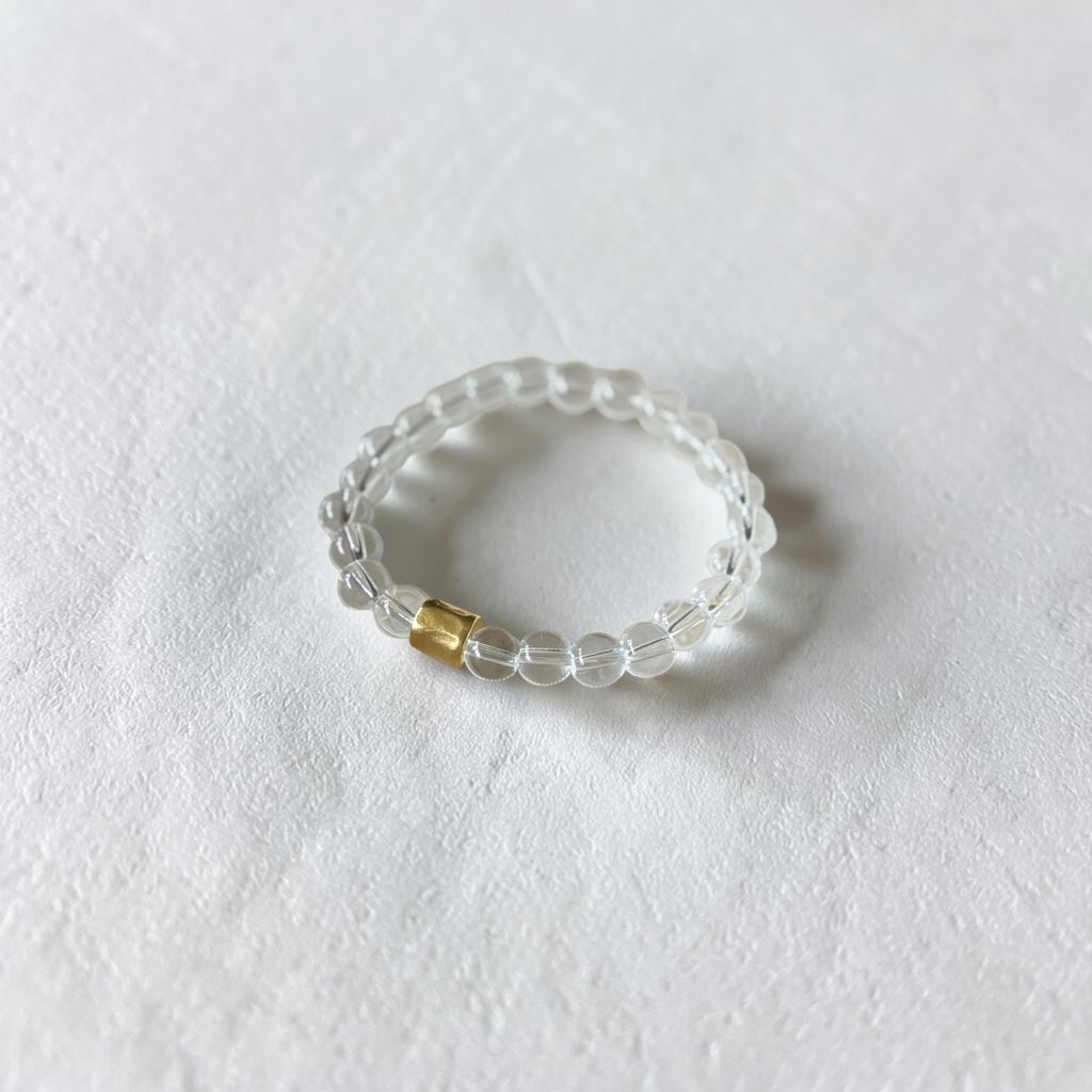 A clear beaded stretch bracelet with a small gold accent bead, photographed on a textured white surface.