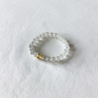A clear beaded stretch bracelet with a small gold accent bead, photographed on a textured white surface.