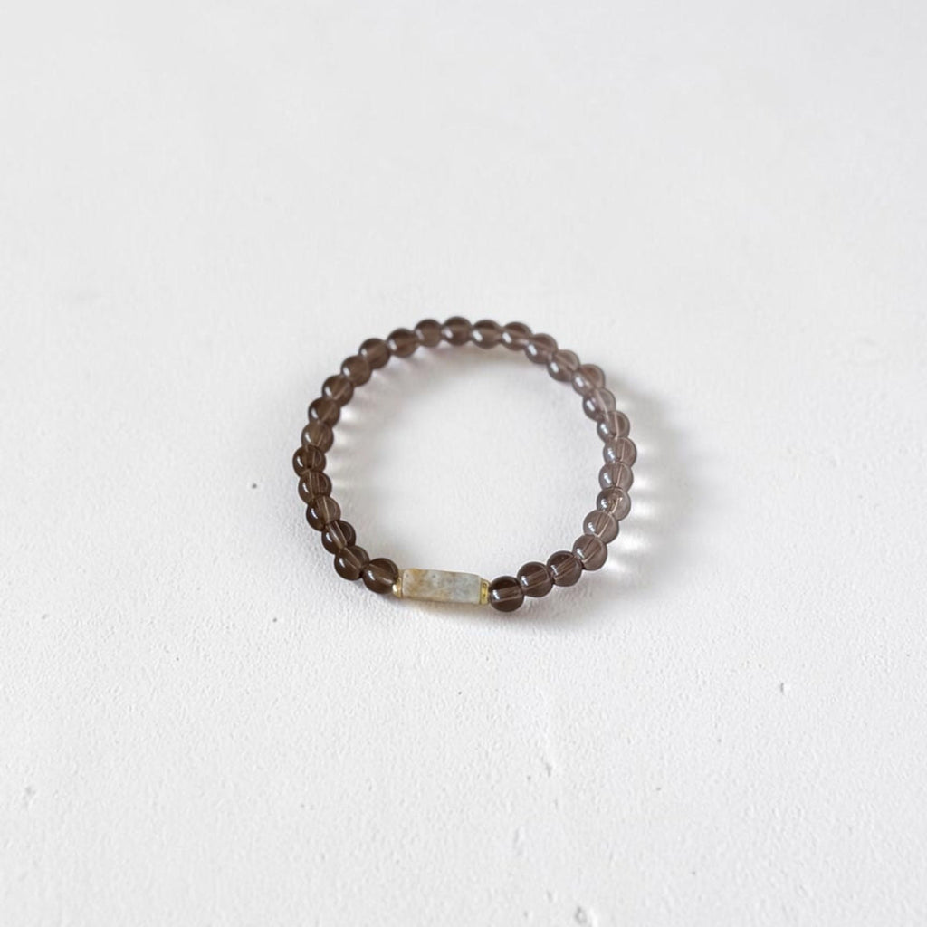 A beaded stretch ring featuring dark brown translucent beads and a small central iridescent white rectangular accent bead, displayed on a clean white surface.