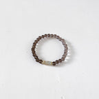 A beaded stretch ring featuring dark brown translucent beads and a small central iridescent white rectangular accent bead, displayed on a clean white surface.