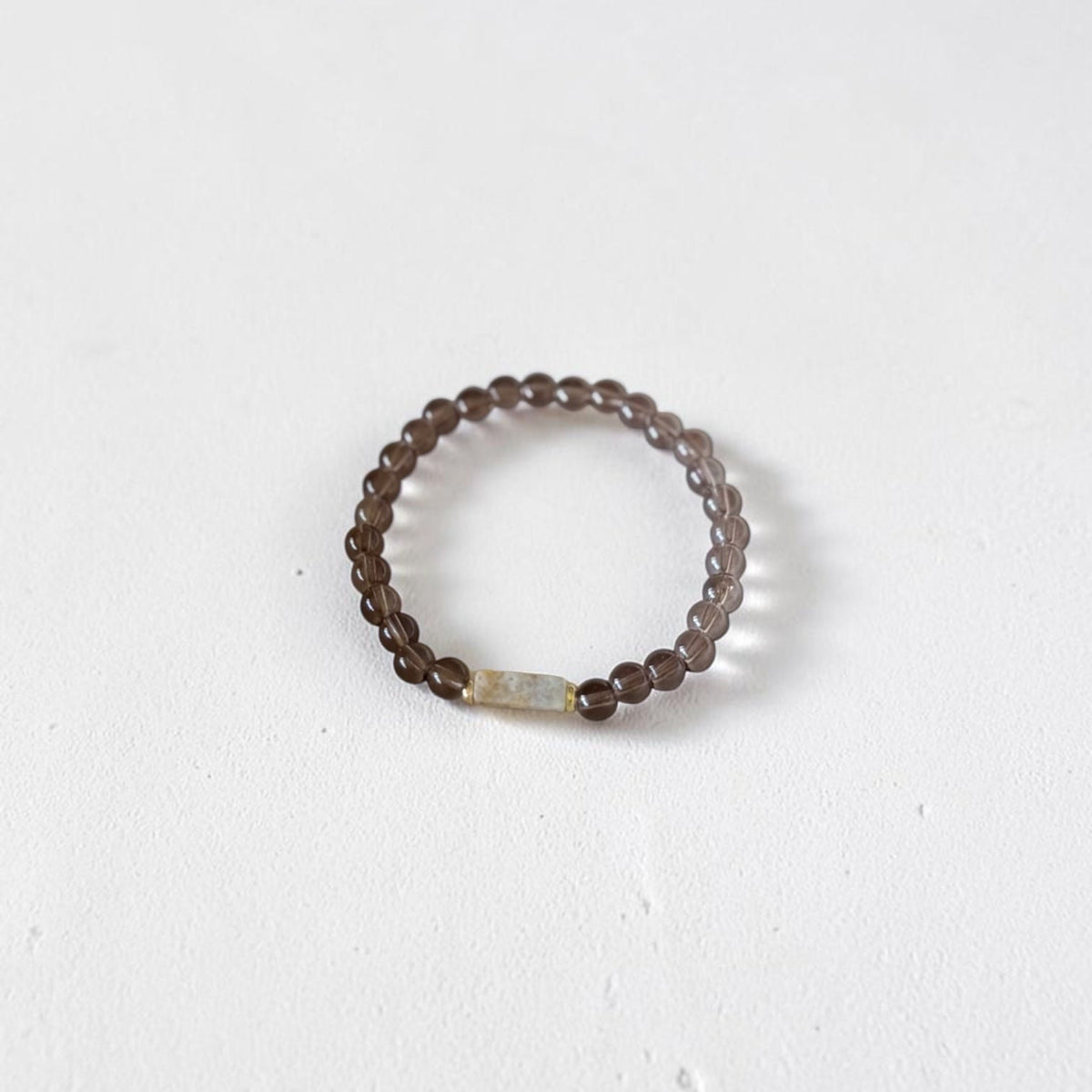 A beaded stretch ring featuring dark brown translucent beads and a small central iridescent white rectangular accent bead, displayed on a clean white surface.