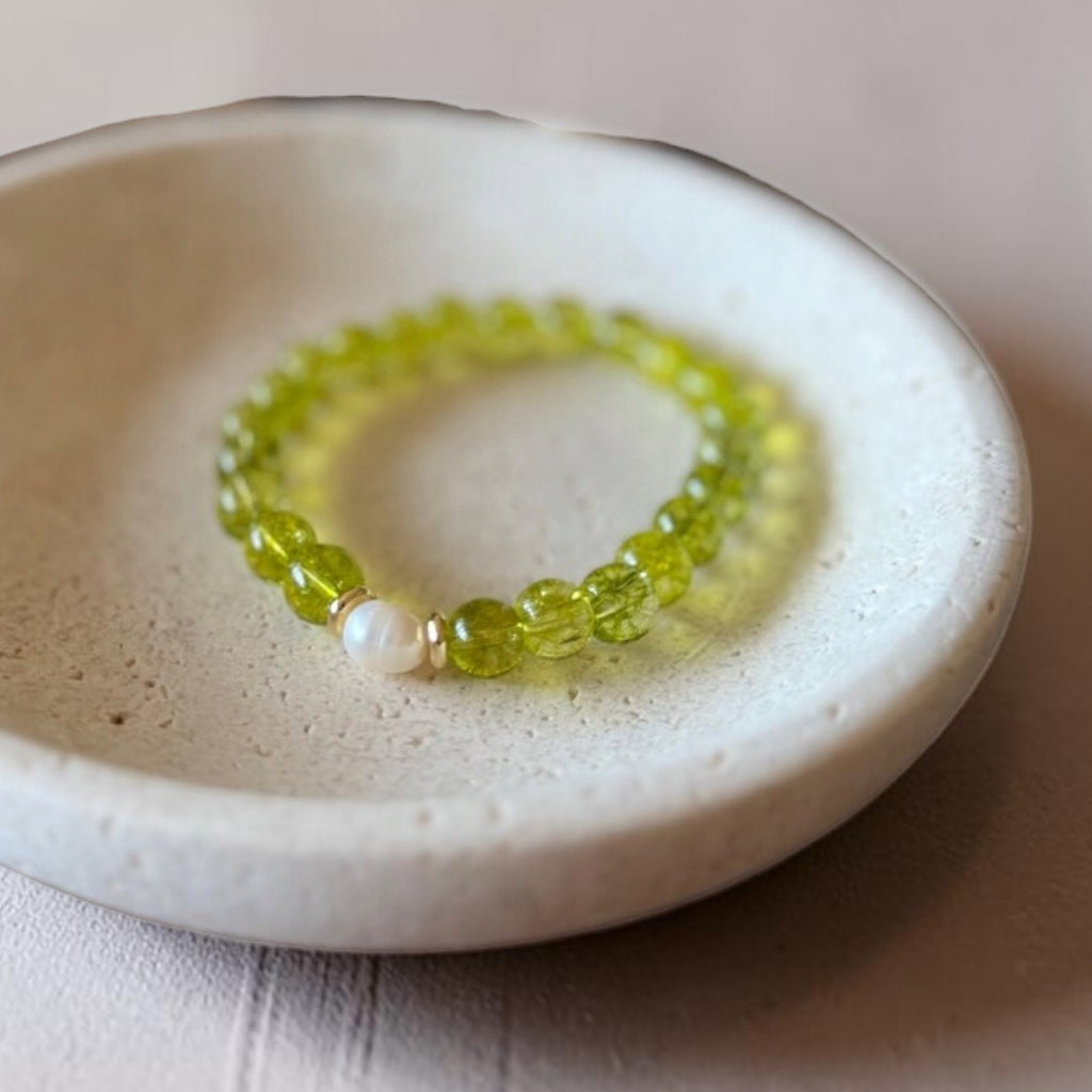 A beaded stretch bracelet with translucent lime green round beads and a single white pearl accent, displayed on a small round ceramic dish.