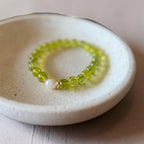 A beaded stretch bracelet with translucent lime green round beads and a single white pearl accent, displayed on a small round ceramic dish.