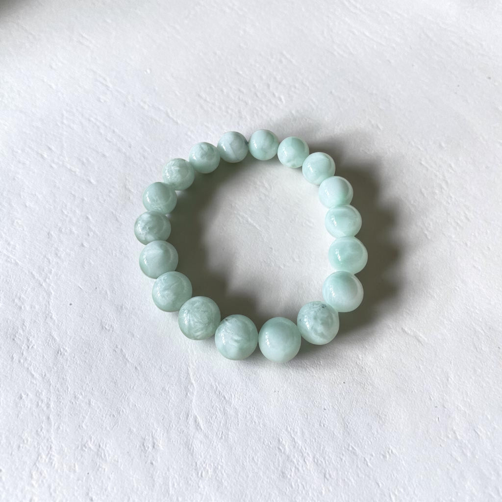 A beaded stretch bracelet made of smooth, light mint green marble-like beads, displayed on a textured white surface.