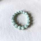 A beaded stretch bracelet made of smooth, light mint green marble-like beads, displayed on a textured white surface.