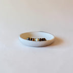 A small beaded stretch bracelet with brown, black, and white beads resting inside a shallow, speckled off-white ceramic dish on a light beige background.