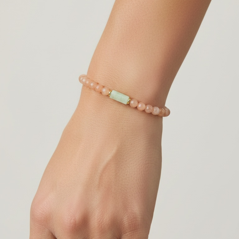 A close-up of a person's wrist wearing a delicate beaded bracelet. The bracelet consists of small, round dusty pink beads with a central, slightly larger pale mint-green rectangular bead.