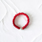 A red beaded stretch bracelet with a single white pearl accent bead, displayed on a textured white background.