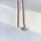 A delicate necklace with a textured pink and gold chain and a single round white pearl bead, resting on a white textured surface with soft shadows.