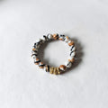 A beaded stretch bracelet featuring marbled white, black, and brown beads, accented by three small gold spacer beads, shown on a light textured background.