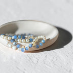 Dish holding a mixture of bracelets. Each bracelet has blue fire agate and pearls.