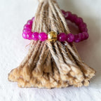 A beaded ring with bright magenta-purple beads and a central gold-toned bead, wrapped around a natural jute tassel on a white textured background.