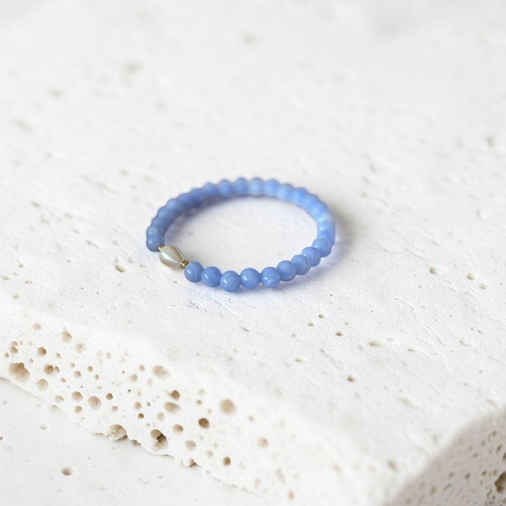 A light blue beaded bracelet with a small silver-toned accent bead, resting on a textured white stone slab.