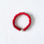 A red beaded bracelet with a small white pearl accent, displayed on a textured white background.