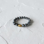 A beaded stretch bracelet featuring dark gray marbled beads and a single faceted gold accent bead, resting on a textured white surface.