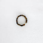 A beaded stretch bracelet featuring polished brown and black tiger's eye beads with a small light blue faceted accent bead, displayed on a textured white surface.