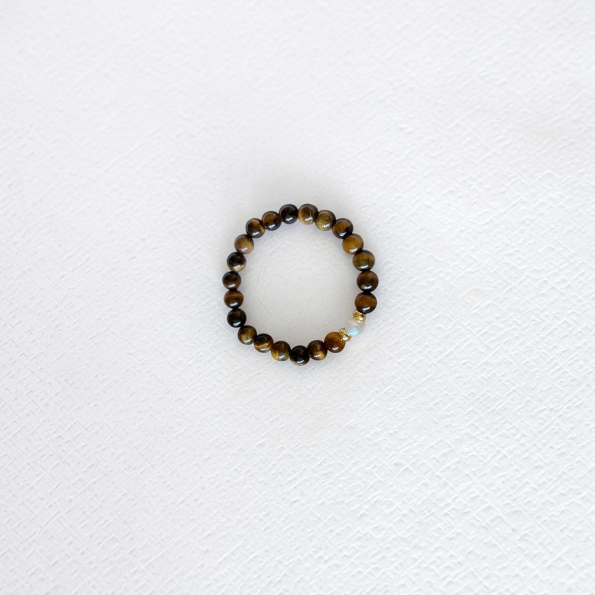 A beaded stretch bracelet featuring polished brown and black tiger's eye beads with a small light blue faceted accent bead, displayed on a textured white surface.