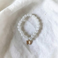 A beaded stretch bracelet made of clear, faceted round beads with a small gold butterfly charm, resting on a textured white fabric background.