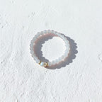 A beaded stretch ring featuring translucent white beads and a small gold-toned accent bead, photographed on a textured white surface with a soft shadow.