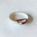 8mm Red Garnet Jade Bead Bracelet with a Gold And Pearl Accent. Accent has a round pearl with gold surrounding the pearl itself. This bracelet is sitting in a dish.