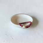 8mm Red Garnet Jade Bead Bracelet with a Gold And Pearl Accent. Accent has a round pearl with gold surrounding the pearl itself. This bracelet is sitting in a dish.