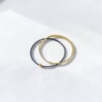 Two thin braided elastic bands, one in dark gray and one in textured gold, with a small gold bead accent on the gray band, displayed on a clean white surface.