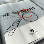 Two thin seed bead bracelets, one orange-red and one dark blue, each with a small gold bead, displayed on an open book with visible Triumph Books branding.