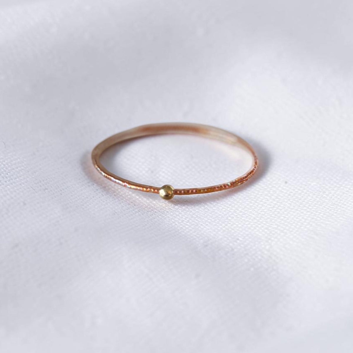 A delicate brown wire bracelet with a small gold bead accent, resting on a textured white fabric background.