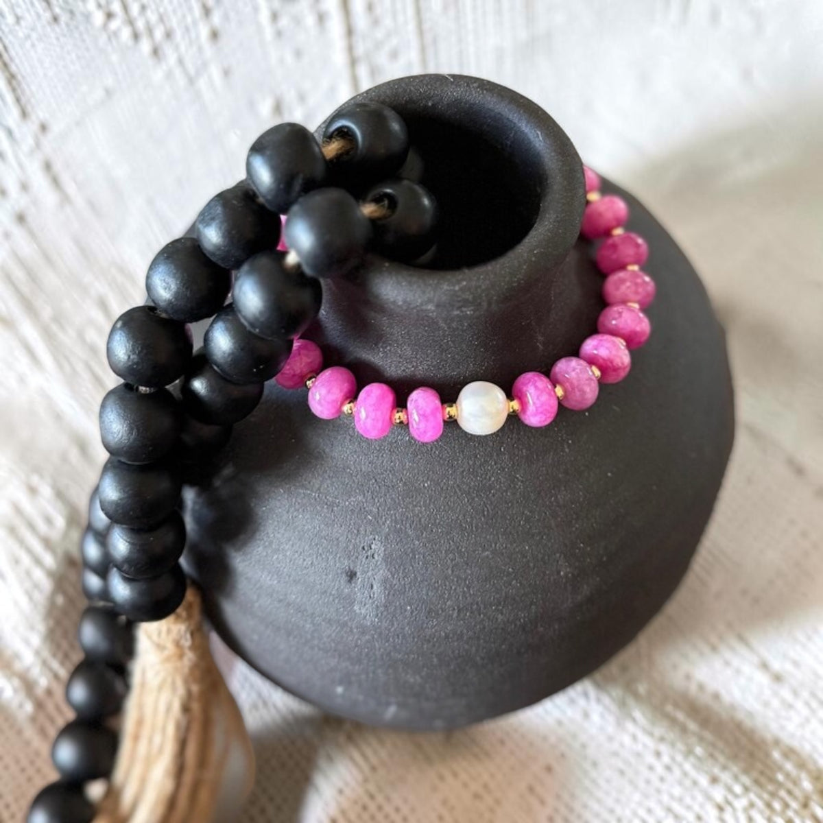 A close-up pink beaded bracelet displayed on a matte black ceramic vase. 