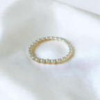A delicate gold spacers adorned with small white pearls, resting on a soft, white satin fabric background.